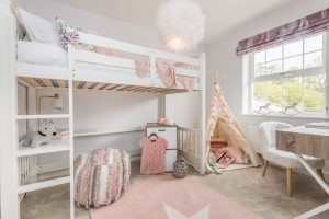 Young girl's bedroom with white loft bed, pink rug, pink throw, fluffy white light, white armchair, wooden desk and pink and beige tent