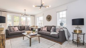 Living room with grey sofas, pink and grey cushions, statement lighting, big clock, wooden coffee table, decorative lamps and ornaments