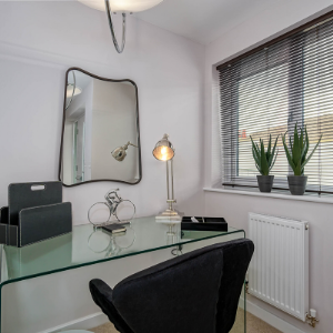 Workspace with glass desk, black chair, silver accessories and big statement mirror